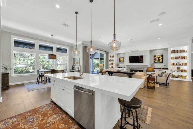 kitchen featuring a sink, dark wood-type flooring, a fireplace, stainless steel dishwasher, and a kitchen island with sink