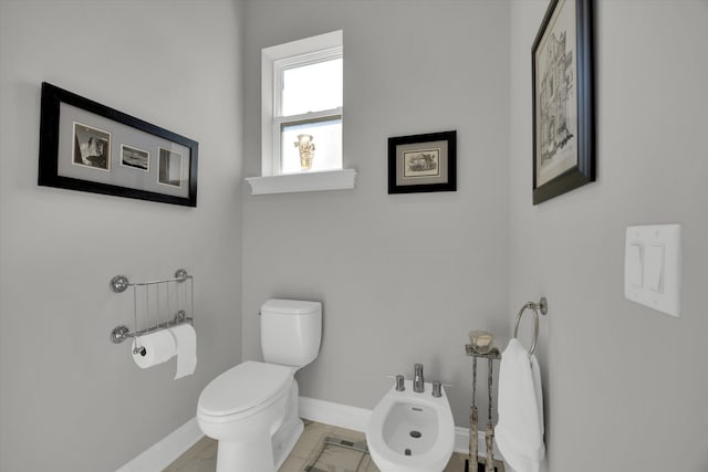 bathroom with toilet, a bidet, and baseboards