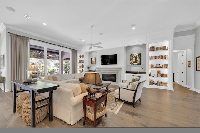 living area with crown molding, recessed lighting, wood finished floors, a glass covered fireplace, and a ceiling fan