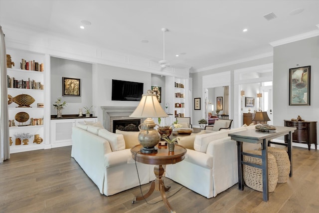 living area with a fireplace, crown molding, wood finished floors, and visible vents