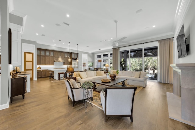 living area featuring crown molding, recessed lighting, a ceiling fan, and light wood-style floors