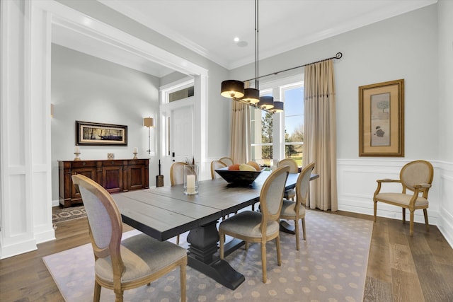 dining area featuring dark wood finished floors, a decorative wall, an inviting chandelier, and ornamental molding