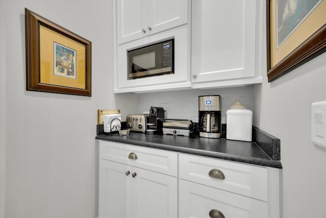 kitchen with built in microwave, backsplash, white cabinetry, and dark countertops