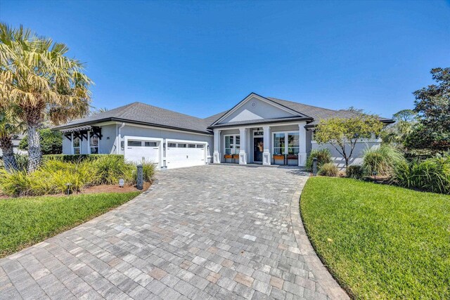 view of front of house with decorative driveway, a front yard, an attached garage, and stucco siding