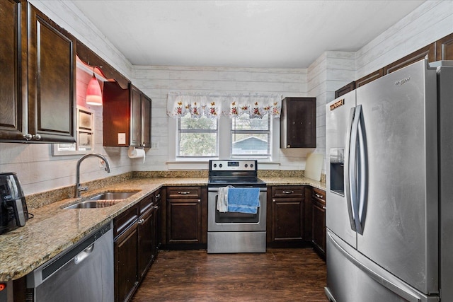 kitchen featuring appliances with stainless steel finishes, light stone counters, sink, dark hardwood / wood-style floors, and wood walls