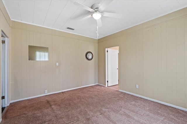 carpeted spare room featuring ceiling fan, wood walls, and ornamental molding