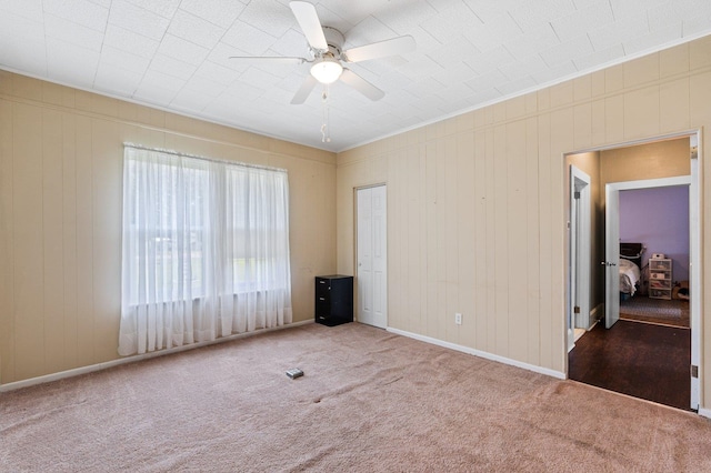 carpeted spare room with ceiling fan and wood walls