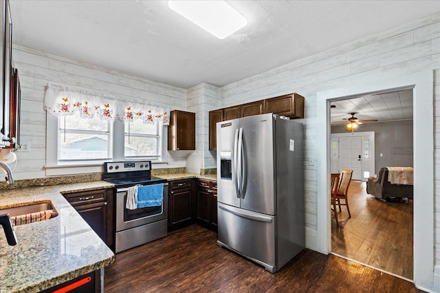 kitchen with dark wood-type flooring, stainless steel appliances, wooden walls, and sink