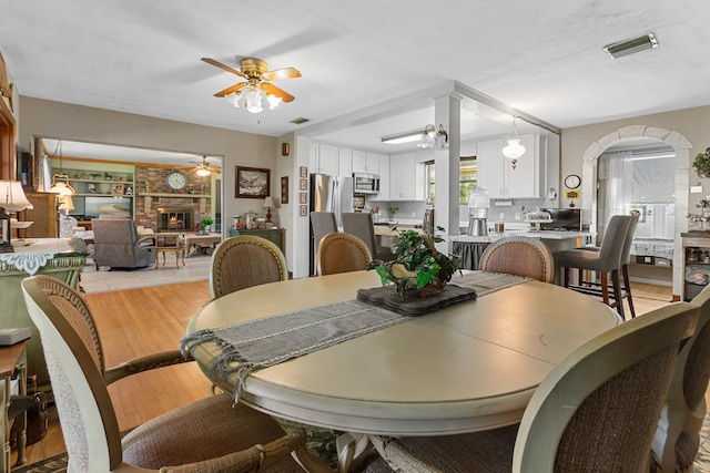 dining space featuring a fireplace, light hardwood / wood-style floors, and ceiling fan