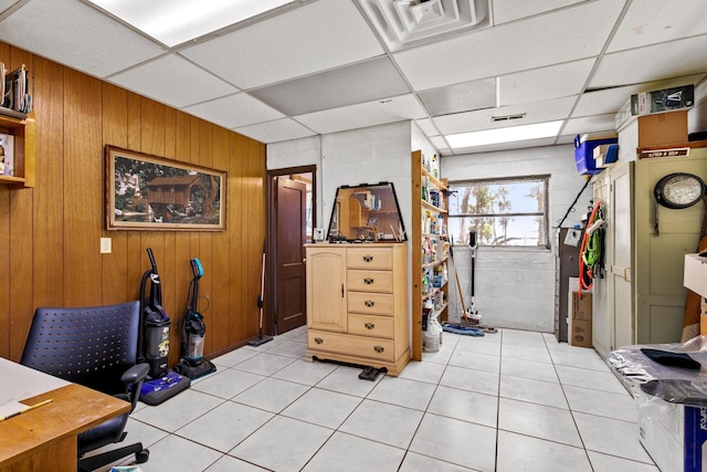 office space with a paneled ceiling, wooden walls, and light tile patterned floors