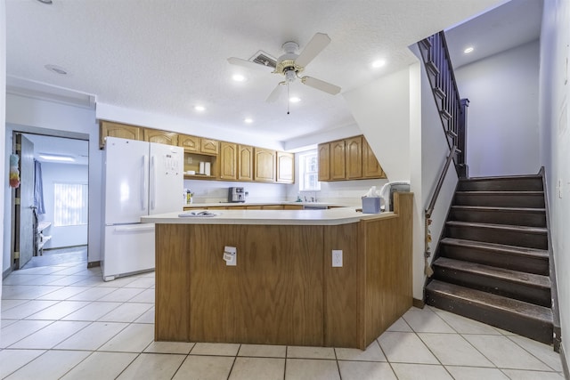 kitchen with ceiling fan, kitchen peninsula, white fridge, a textured ceiling, and light tile patterned floors