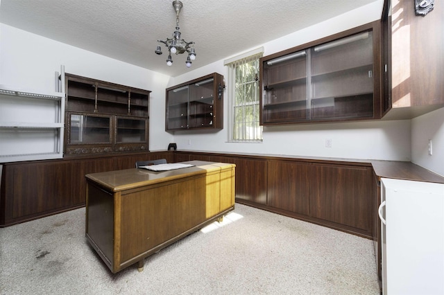 unfurnished office featuring wooden walls, light colored carpet, a textured ceiling, and a notable chandelier