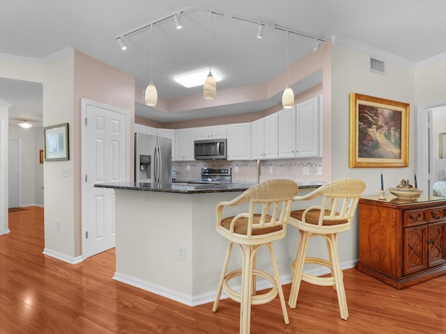 kitchen with hanging light fixtures, stainless steel appliances, white cabinets, and light wood-type flooring