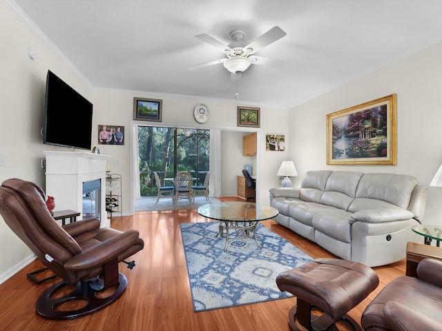 living room with baseboards, a ceiling fan, a glass covered fireplace, light wood-style flooring, and ornamental molding