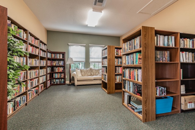 living area featuring baseboards, visible vents, wall of books, carpet, and a textured ceiling