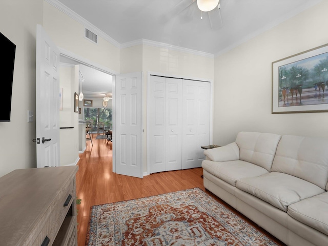 living room with ceiling fan, light wood finished floors, visible vents, and crown molding