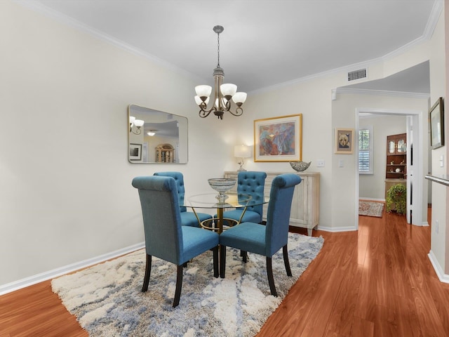 dining area with a chandelier, wood finished floors, visible vents, baseboards, and ornamental molding