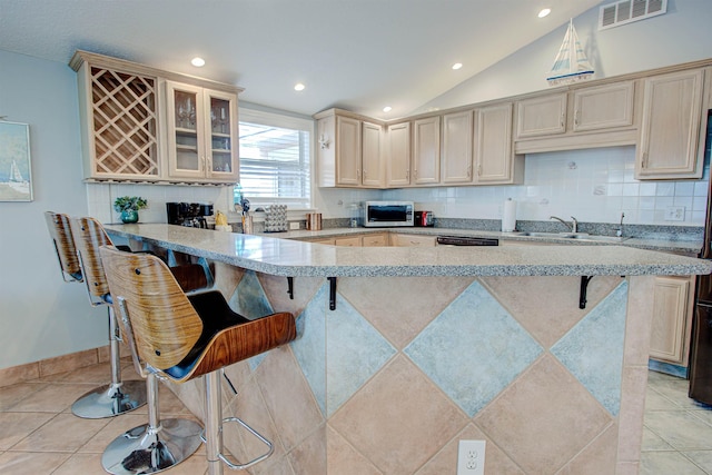 kitchen featuring light stone countertops, sink, a breakfast bar area, decorative backsplash, and light tile patterned floors