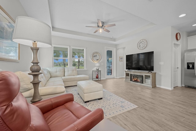 living room featuring light hardwood / wood-style floors, a raised ceiling, and ceiling fan