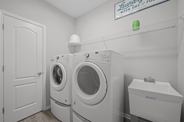 clothes washing area with light hardwood / wood-style floors, separate washer and dryer, and sink