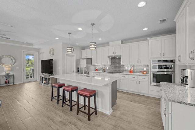 kitchen featuring white cabinets, a center island with sink, hanging light fixtures, light hardwood / wood-style floors, and stainless steel appliances