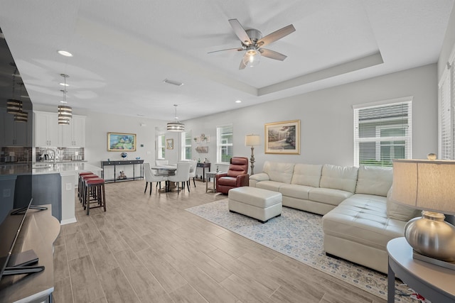 living room featuring light wood-type flooring, a tray ceiling, and ceiling fan