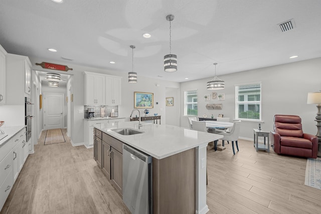 kitchen featuring white cabinets, sink, an island with sink, decorative light fixtures, and stainless steel appliances