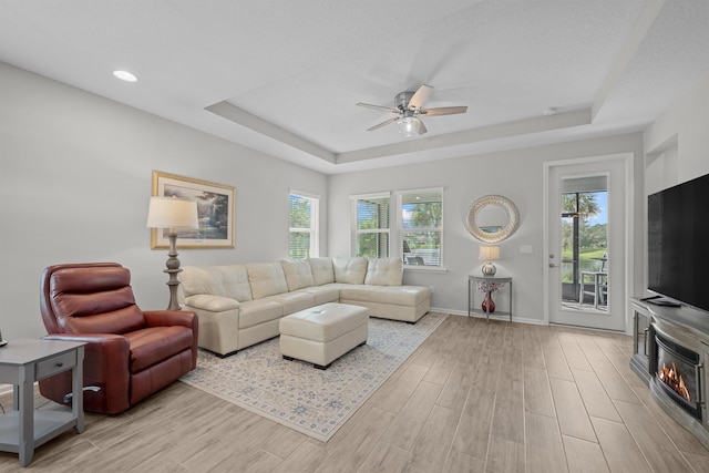 living room with a raised ceiling, light hardwood / wood-style flooring, and ceiling fan