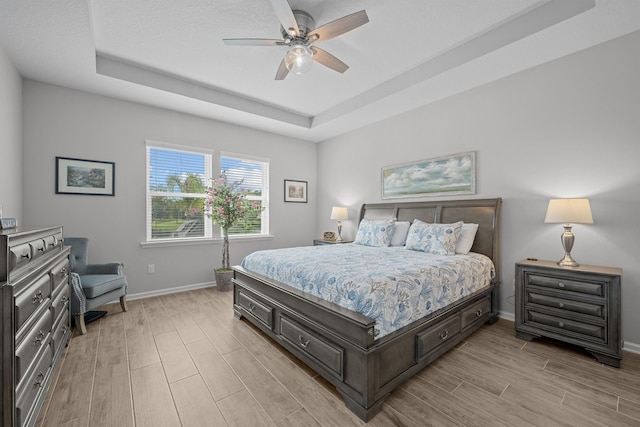 bedroom with light hardwood / wood-style floors, a raised ceiling, and ceiling fan