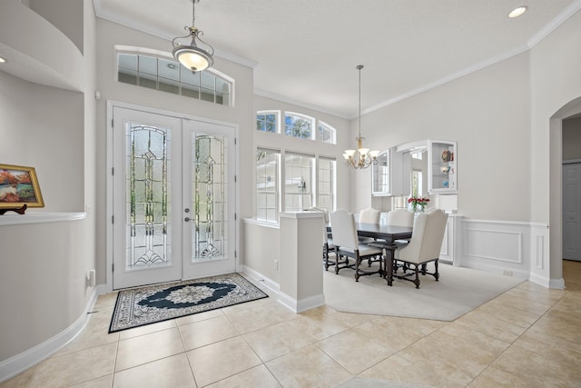 tiled foyer entrance with a notable chandelier, crown molding, and french doors