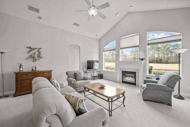 carpeted living room with ceiling fan, a fireplace, and high vaulted ceiling