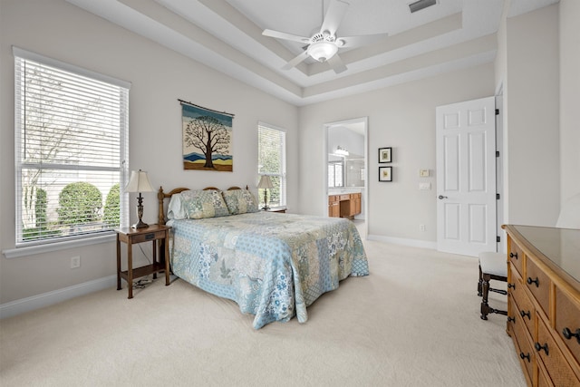 carpeted bedroom featuring a raised ceiling, ensuite bathroom, ceiling fan, and multiple windows