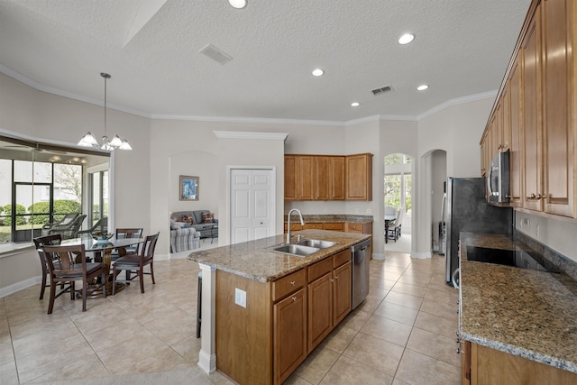 kitchen featuring sink, appliances with stainless steel finishes, light stone counters, a center island with sink, and decorative light fixtures