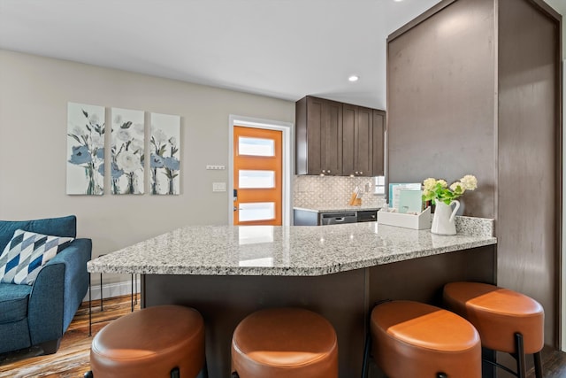 kitchen featuring a breakfast bar, light hardwood / wood-style flooring, kitchen peninsula, decorative backsplash, and dark brown cabinets