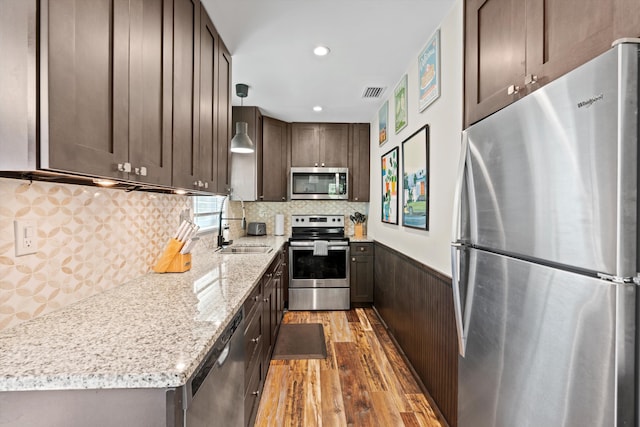 kitchen with pendant lighting, dark wood-type flooring, sink, light stone countertops, and stainless steel appliances