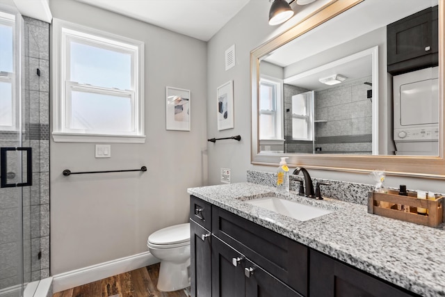 bathroom with toilet, vanity, a shower with shower door, stacked washer and clothes dryer, and hardwood / wood-style flooring