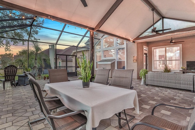 patio terrace at dusk featuring a lanai, lofted ceiling with beams, and ceiling fan