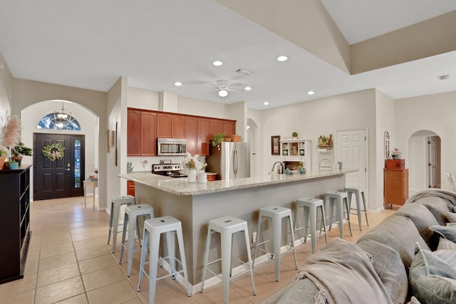 kitchen featuring light tile patterned floors, a breakfast bar, ceiling fan, appliances with stainless steel finishes, and a center island with sink