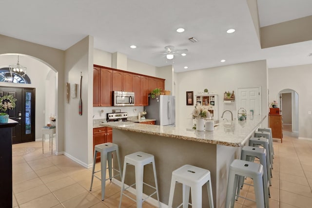 kitchen featuring stainless steel appliances, light stone countertops, a kitchen island with sink, and a kitchen breakfast bar