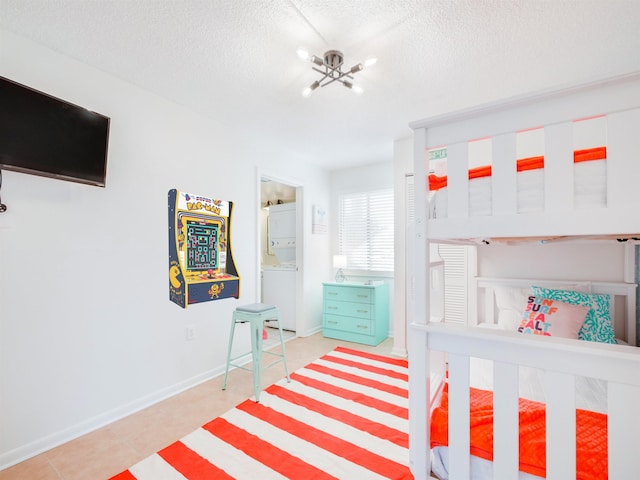 bedroom with an inviting chandelier, baseboards, stacked washer and clothes dryer, and a textured ceiling