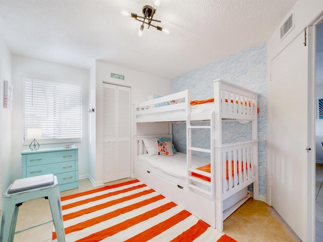 bedroom with light tile patterned floors, visible vents, wallpapered walls, a closet, and a textured ceiling