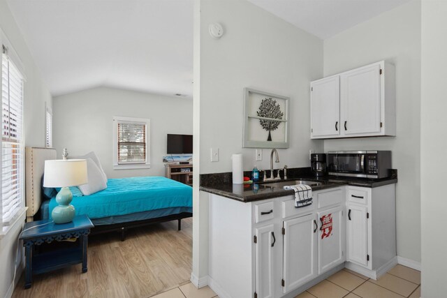 kitchen featuring a sink, stainless steel microwave, dark countertops, white cabinetry, and lofted ceiling