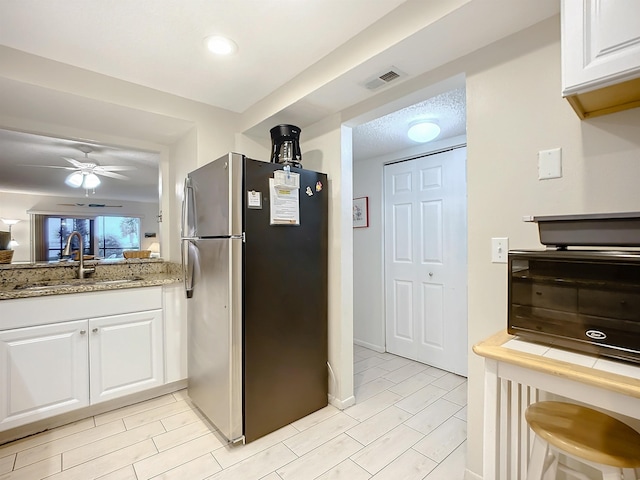 kitchen with ceiling fan, white cabinetry, sink, and stainless steel refrigerator