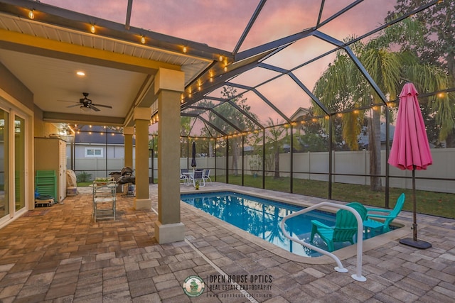 pool at dusk featuring a lanai, ceiling fan, and a patio