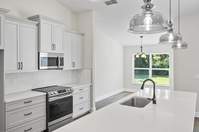 kitchen with backsplash, sink, appliances with stainless steel finishes, decorative light fixtures, and dark hardwood / wood-style flooring