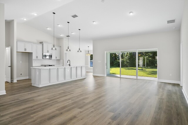 kitchen with dark wood-type flooring, a center island with sink, white cabinetry, hanging light fixtures, and lofted ceiling