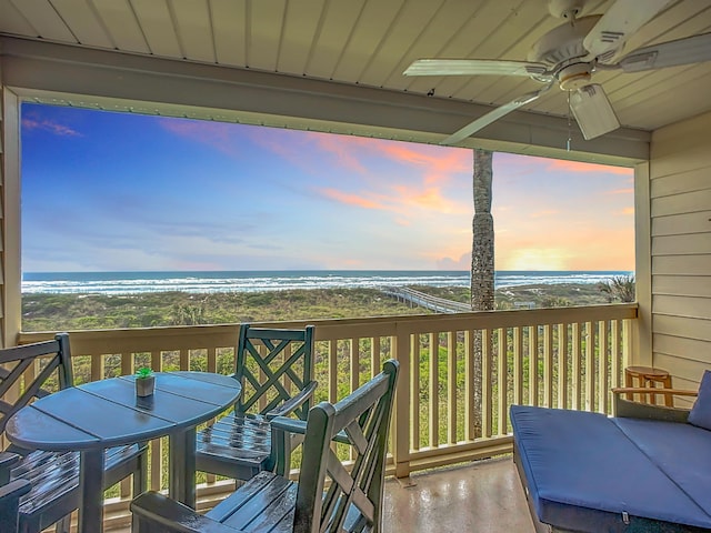 deck at dusk with ceiling fan, a water view, and a view of the beach