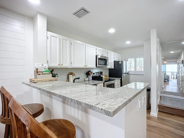 kitchen with stainless steel appliances, tasteful backsplash, kitchen peninsula, a kitchen bar, and white cabinets