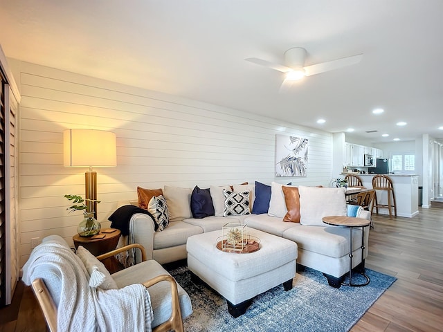 living room featuring ceiling fan, wood-type flooring, and wooden walls