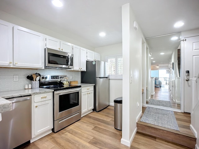 kitchen featuring white cabinetry, light stone counters, backsplash, appliances with stainless steel finishes, and light wood-type flooring